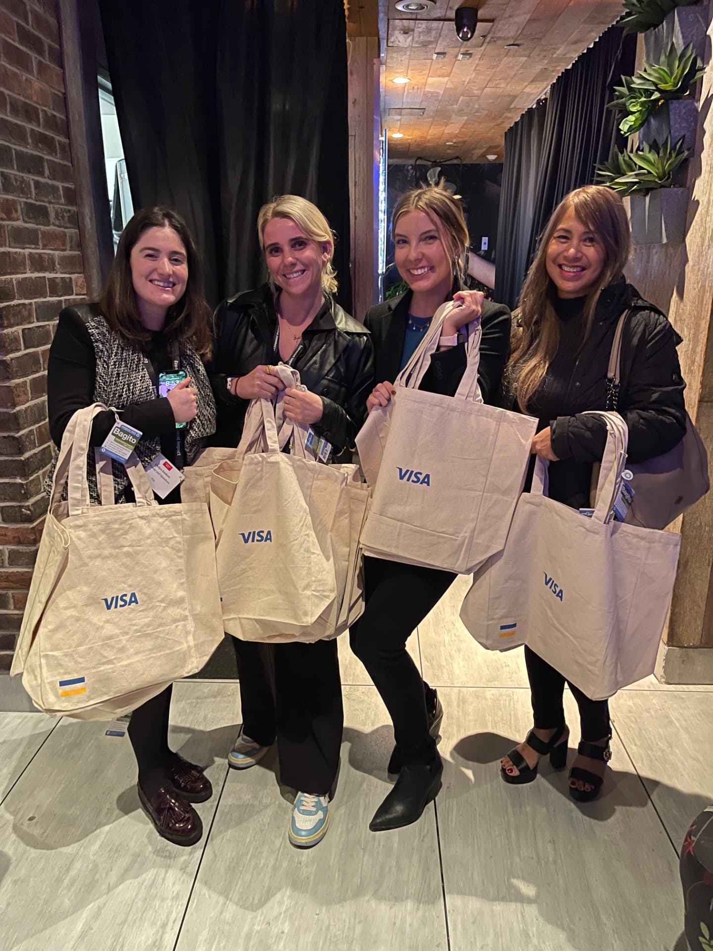 Four guests holding Visa canvas tote bag giveaways at the exit