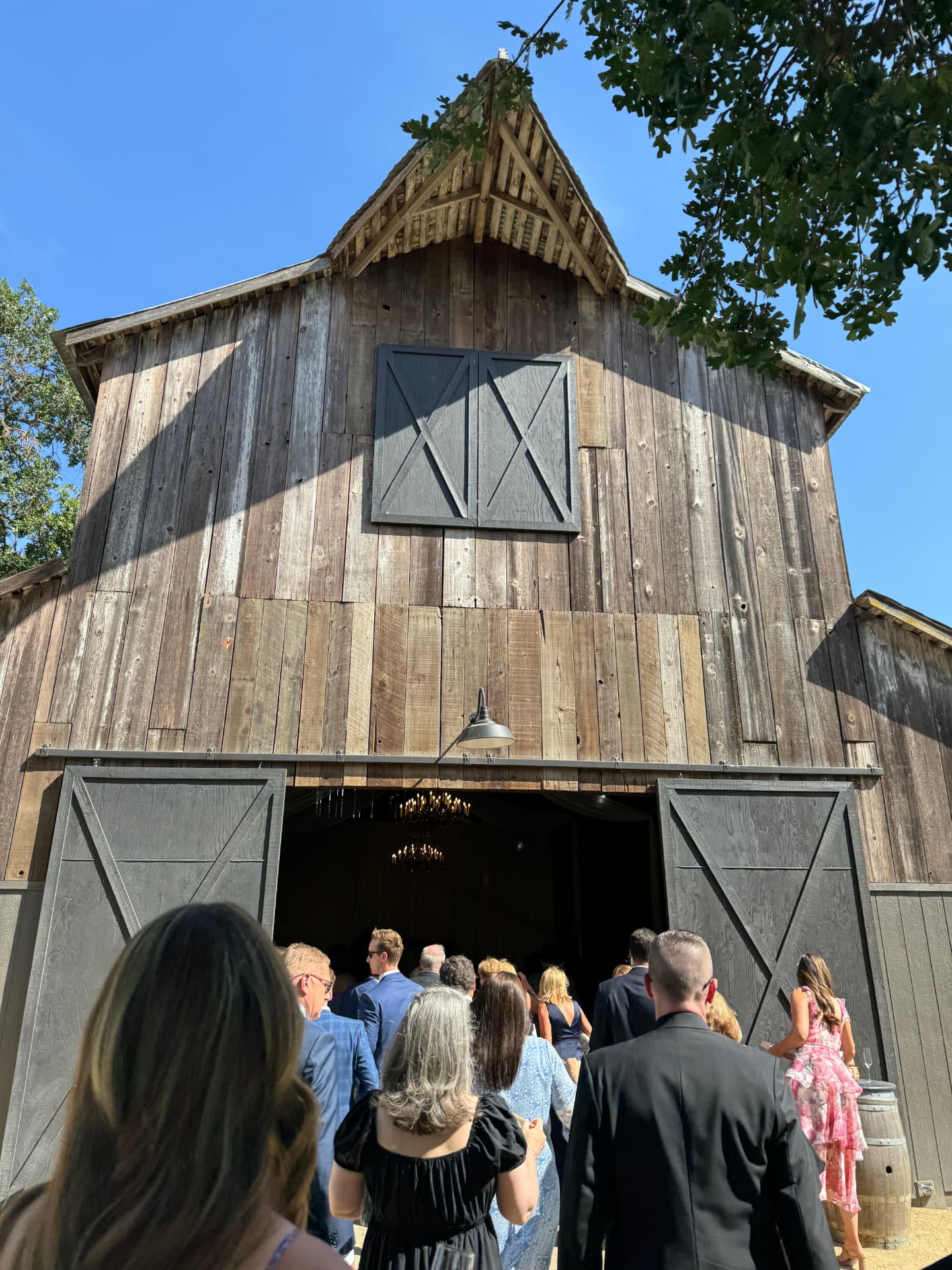 Guests filing into a restored wooden barn lit with chandeliers for the reception