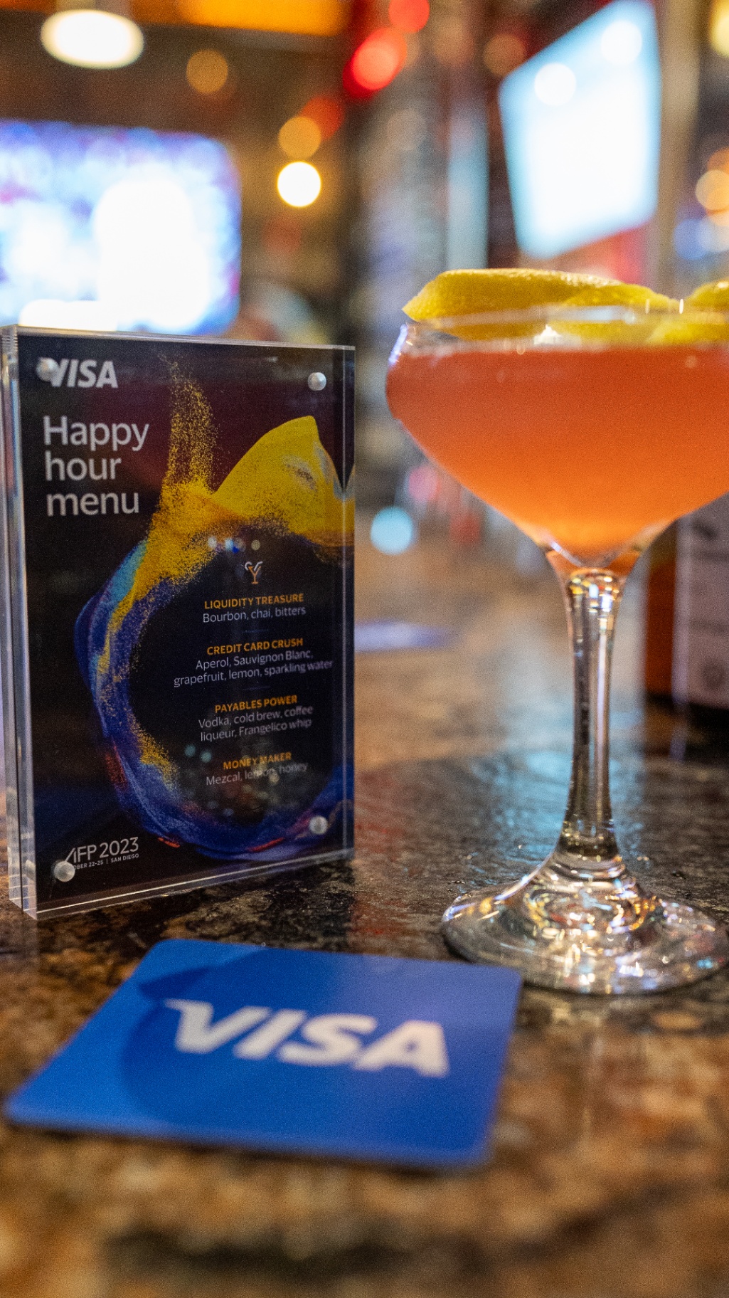 Visa happy hour menu beside a signature cocktail and branded coaster