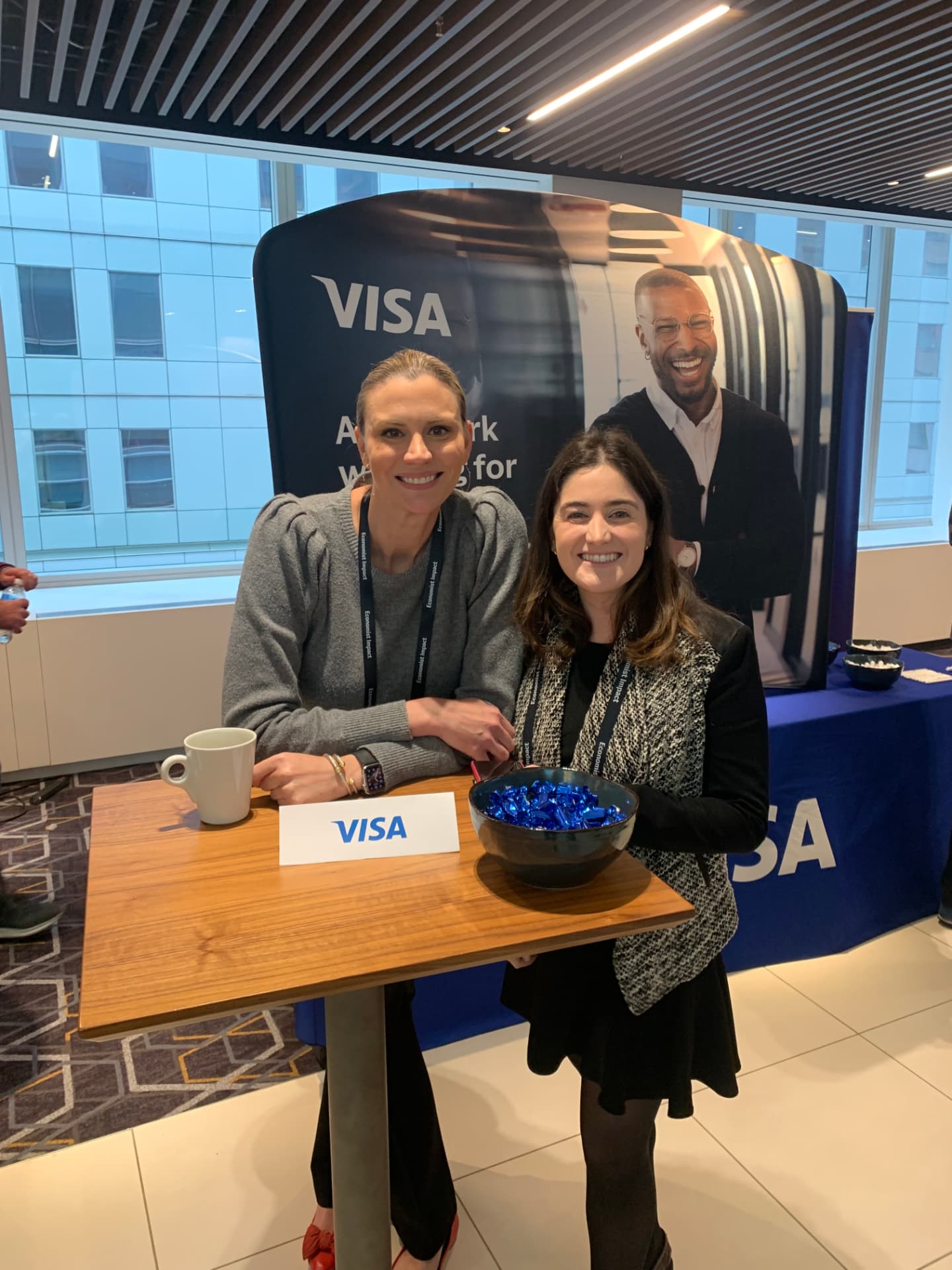 Two attendees seated at a Visa-branded high-top table with candy bowl