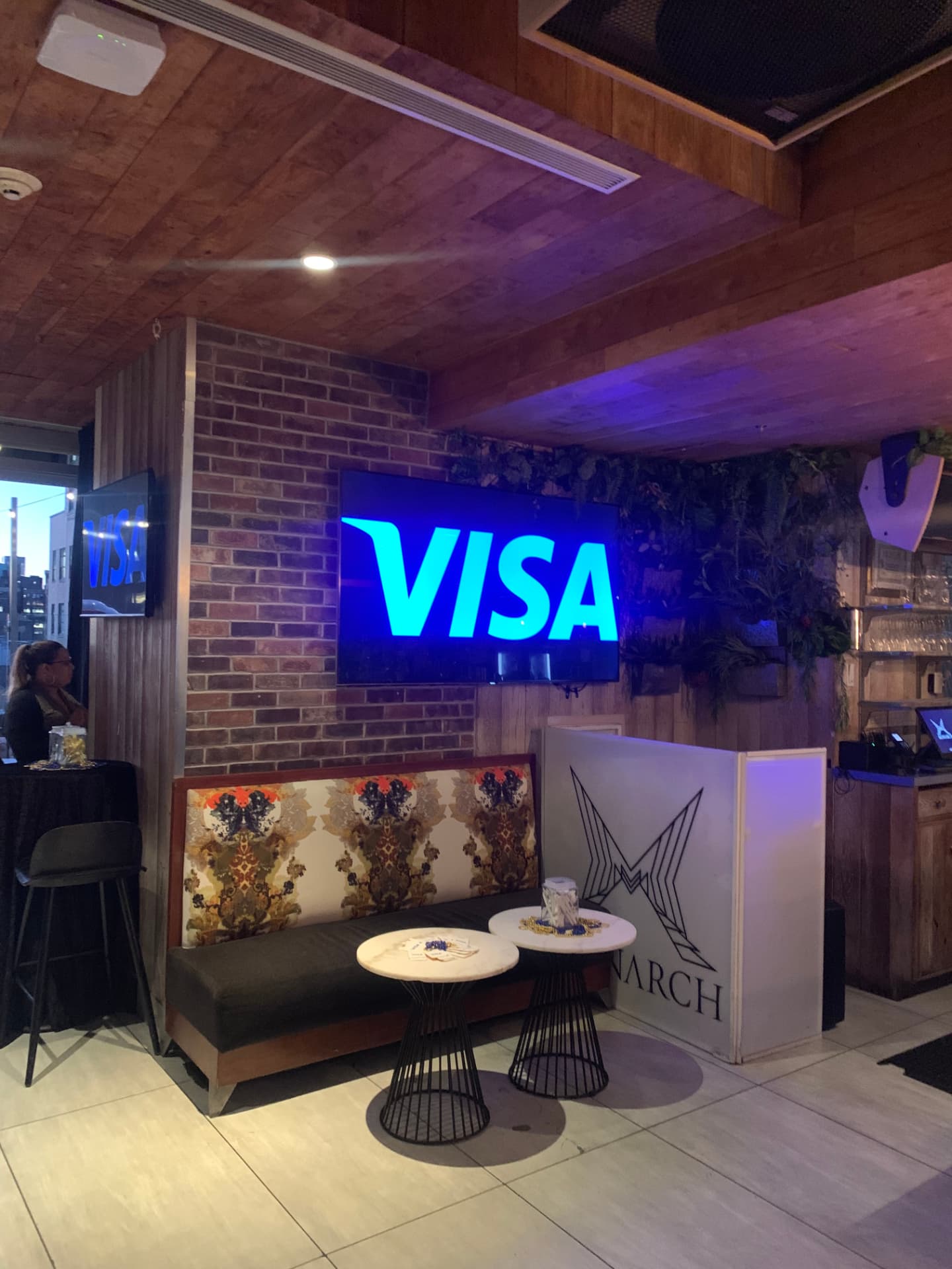 Lounge seating beneath a glowing Visa screen at the Monarch rooftop