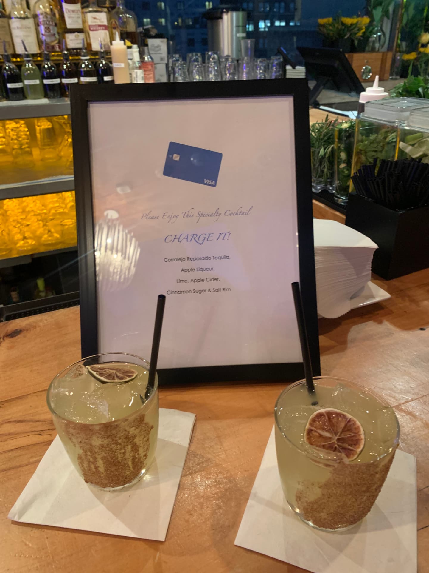 Two 'Charge It!' cocktails with dried lime garnish beside the Visa menu
