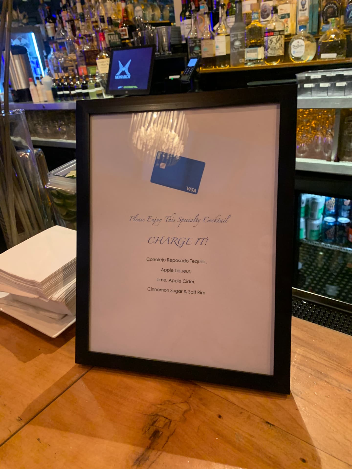 Framed 'Charge It!' Visa specialty cocktail menu on the bar