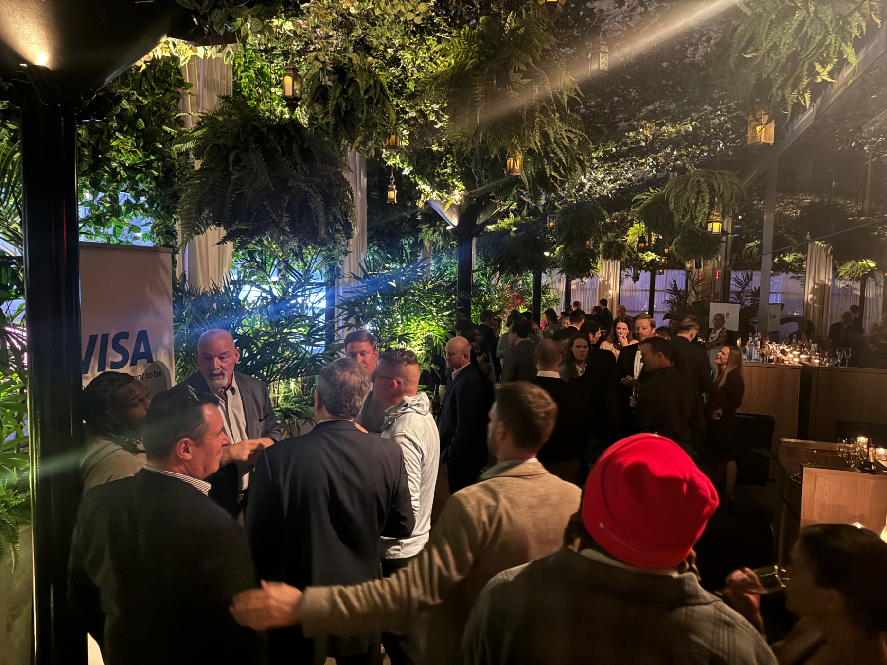 Guests networking under the greenery-and-lantern canopy at the Visa reception