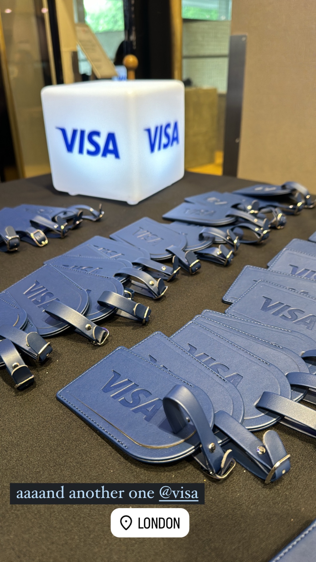Navy Visa leather luggage tags arranged beside a glowing Visa cube in London