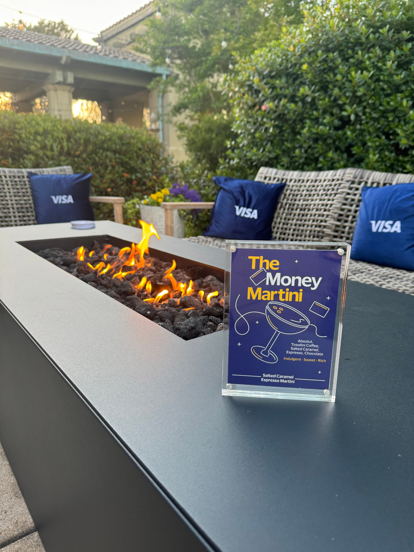 The Money Martini cocktail sign beside a fire table with Visa pillows