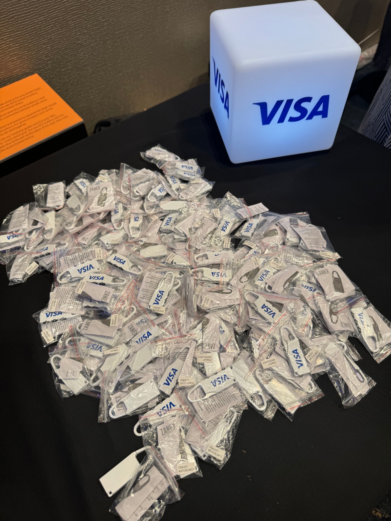 Illuminated Visa cube beside a pile of branded luggage-tag giveaways