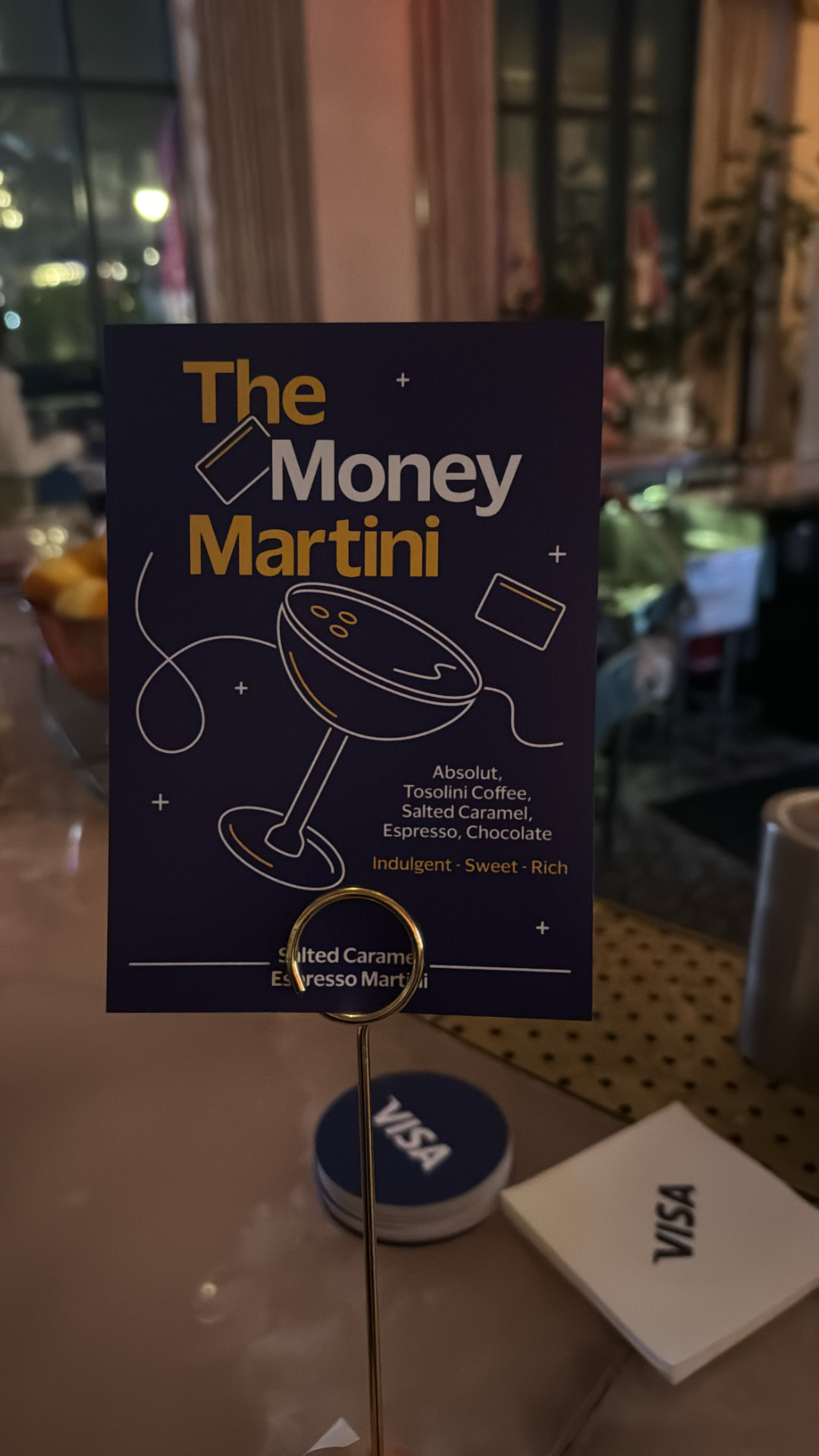 'The Money Martini' cocktail card on a gold stand beside Visa coasters