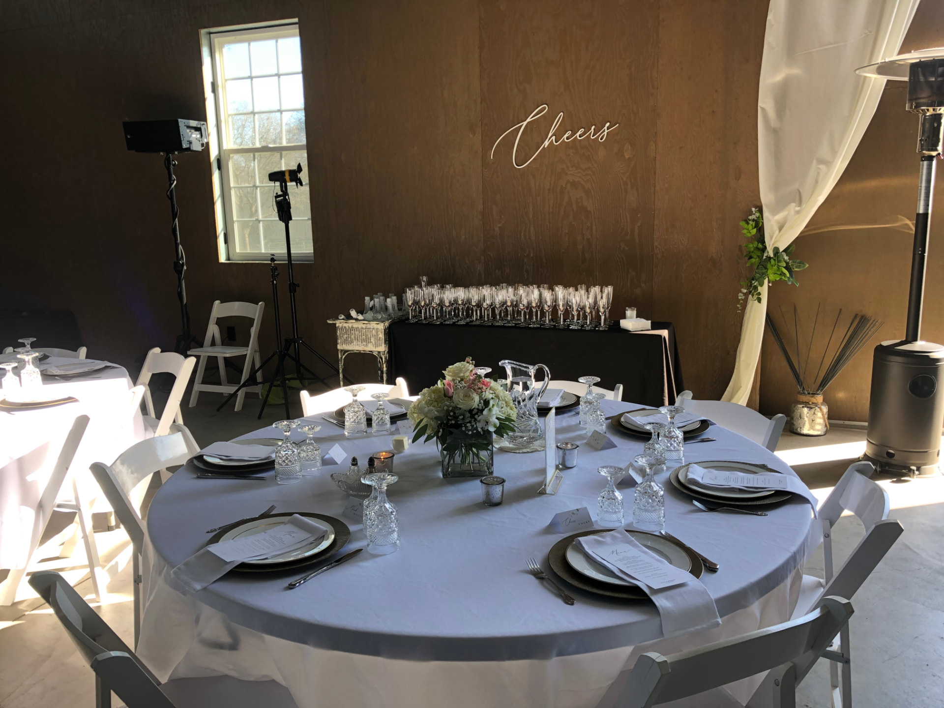 Round table setting with crystal glassware, blush florals and a 'Cheers' wall installation