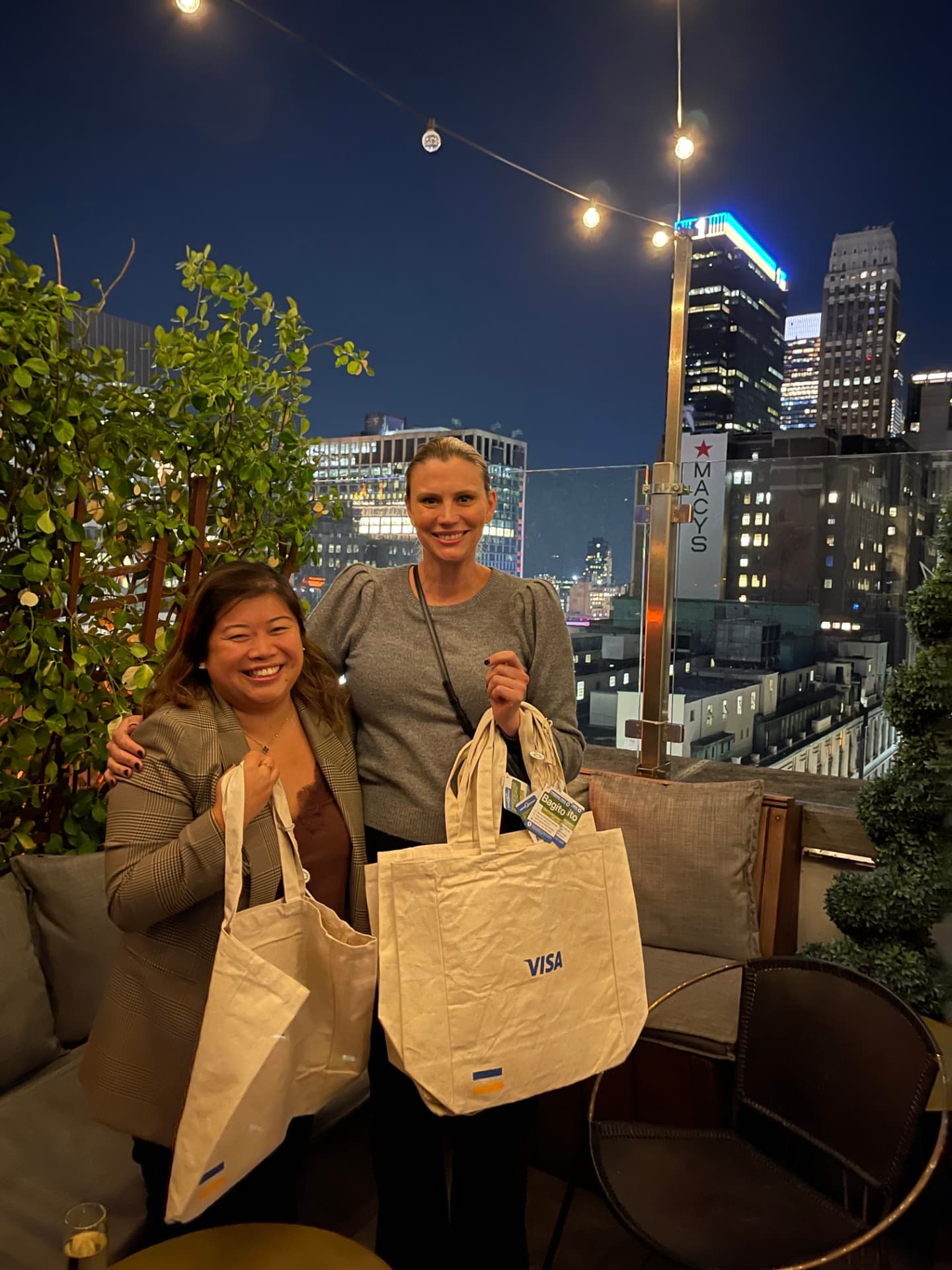 Two guests holding Visa tote bag gifts with the Manhattan skyline behind them