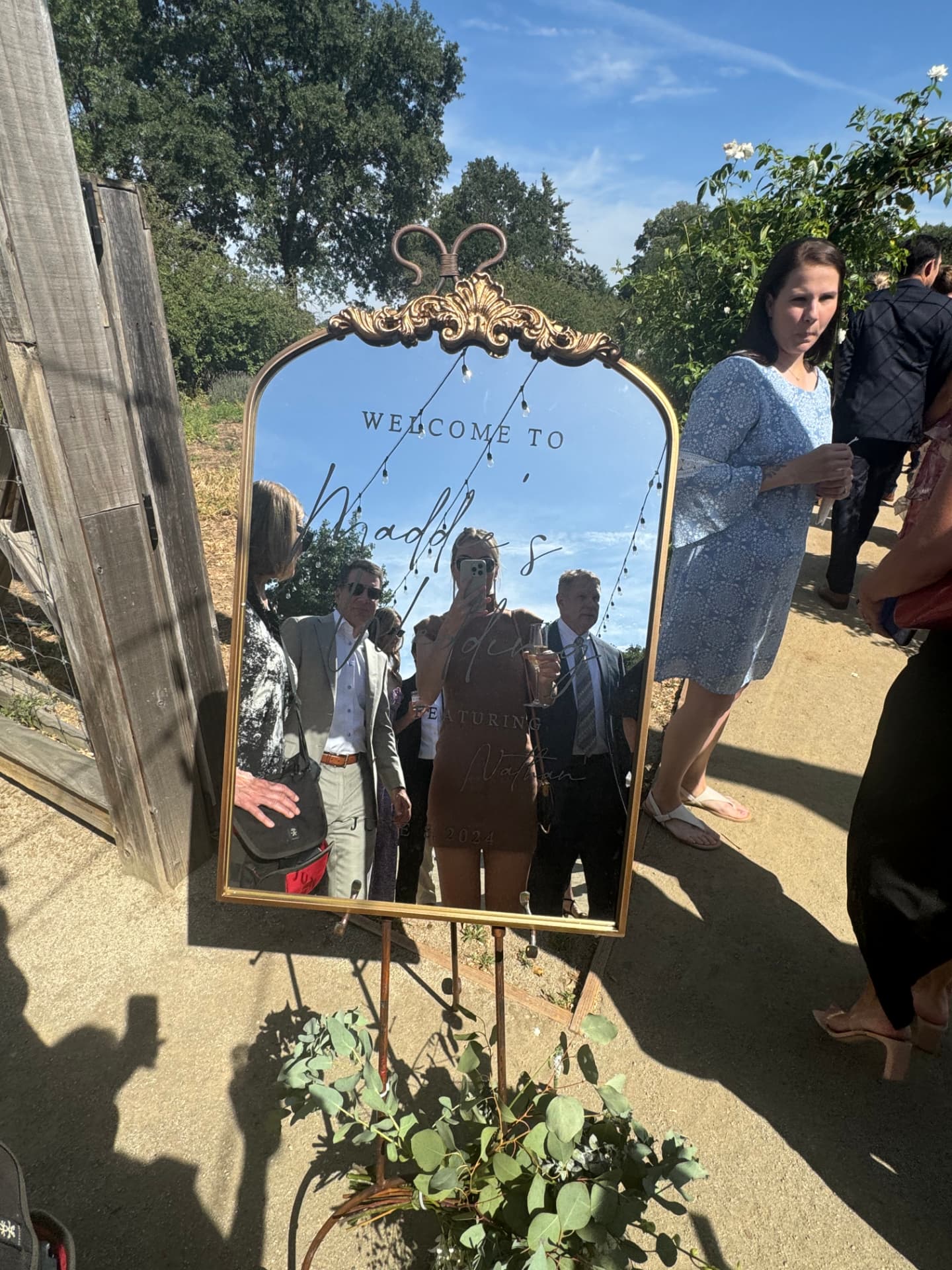 Etched welcome mirror on a gold easel with eucalyptus at the garden entrance