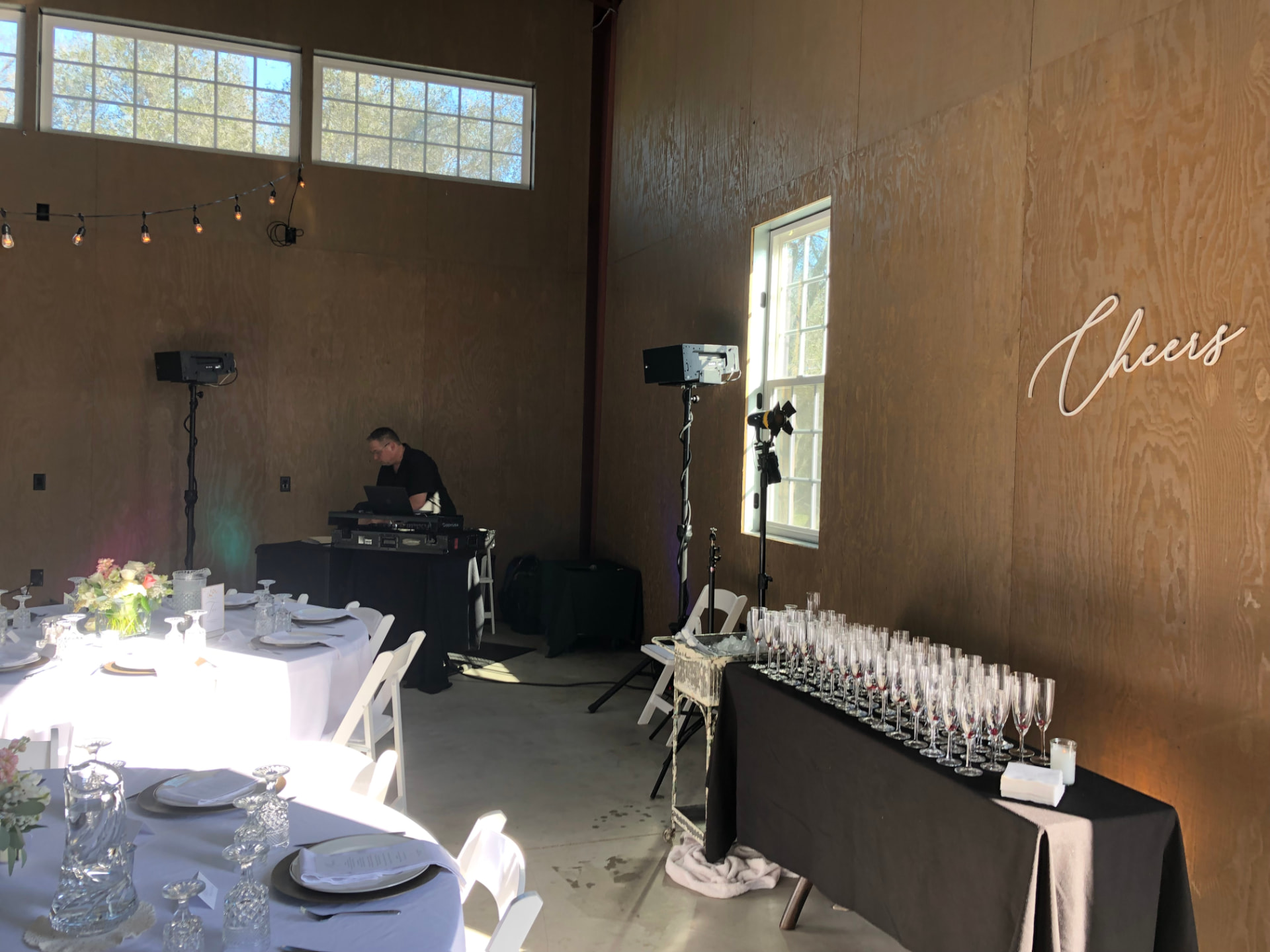 Champagne flutes lined up on a black-draped table beneath a script 'Cheers' sign