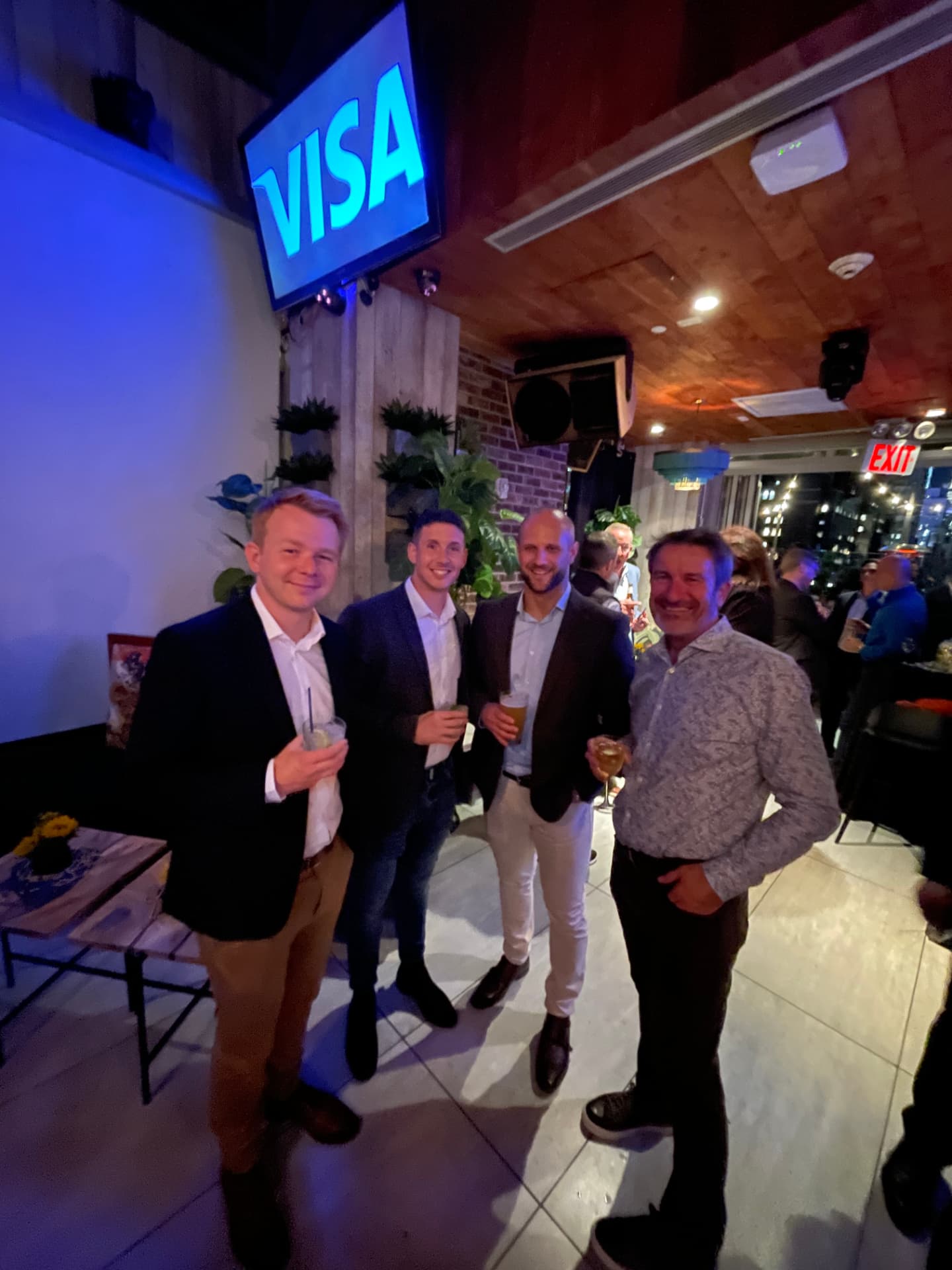 Four guests toasting drinks in front of the Visa screen