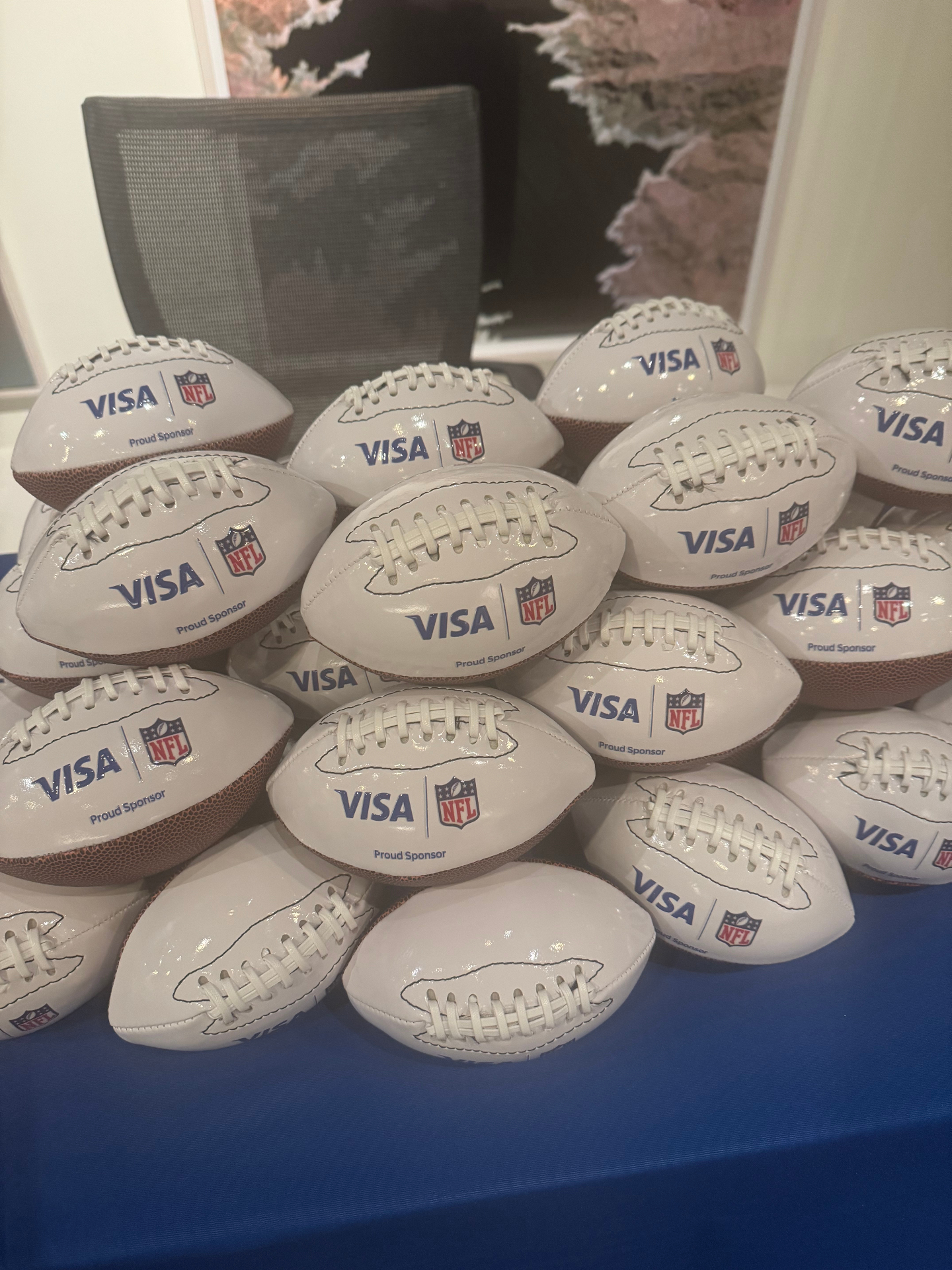 Stack of Visa and NFL co-branded mini footballs on a blue linen table