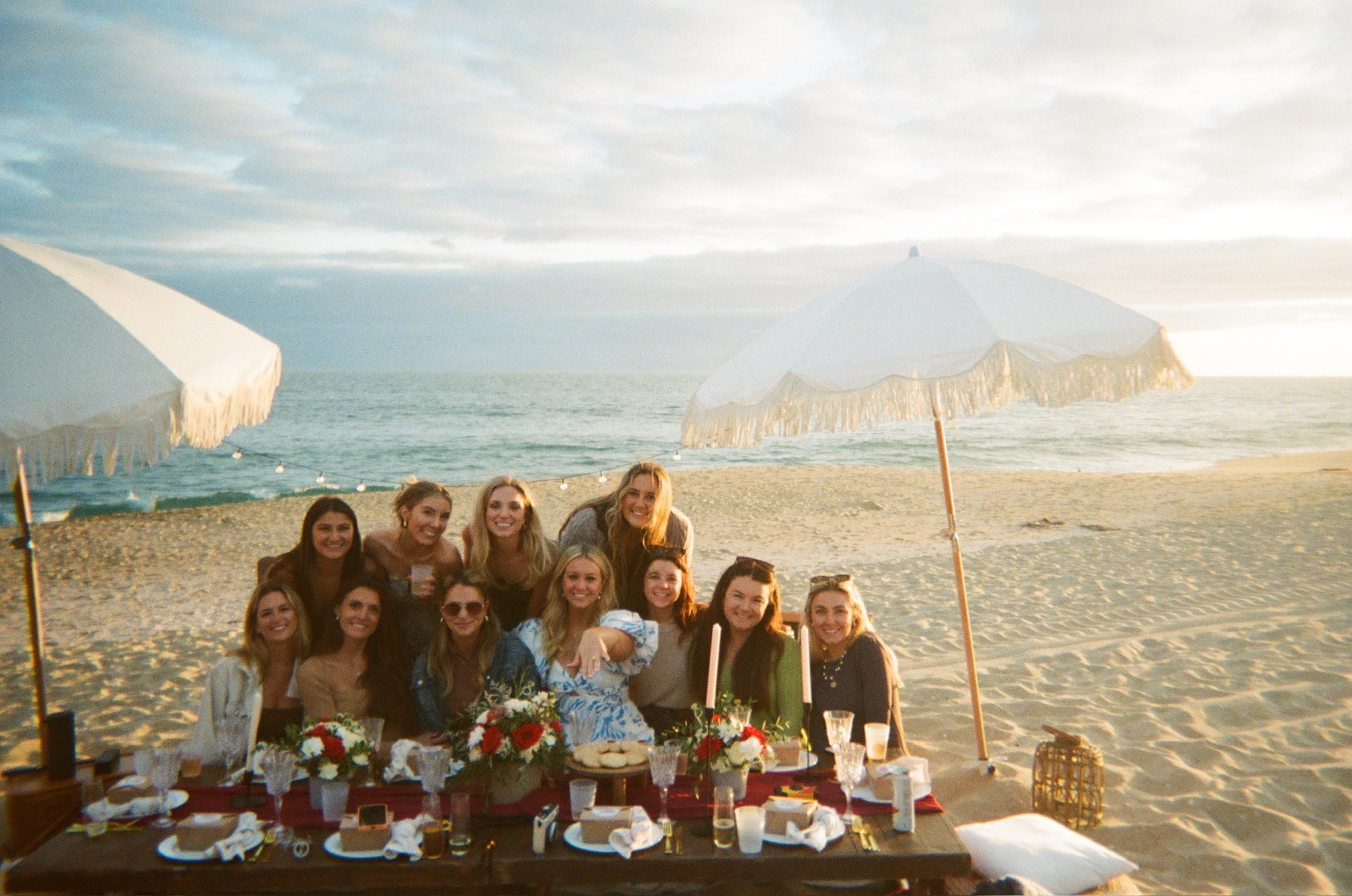 Beach engagement party - group photo of women celebrating at beachside table with umbrellas and floral arrangements