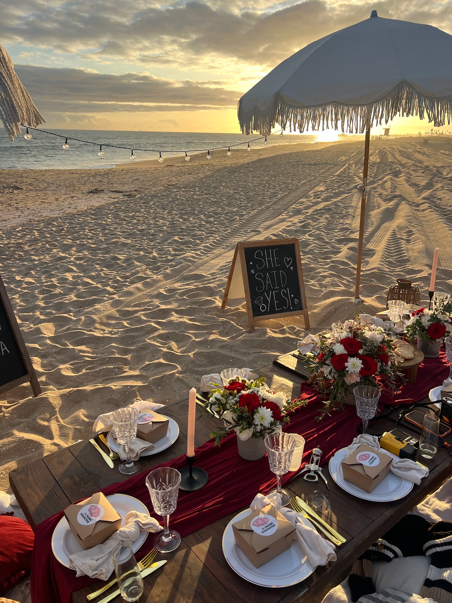 Beach engagement party - stunning golden hour setup with 'SHE SAID YES!' sign, elegant table, and string lights