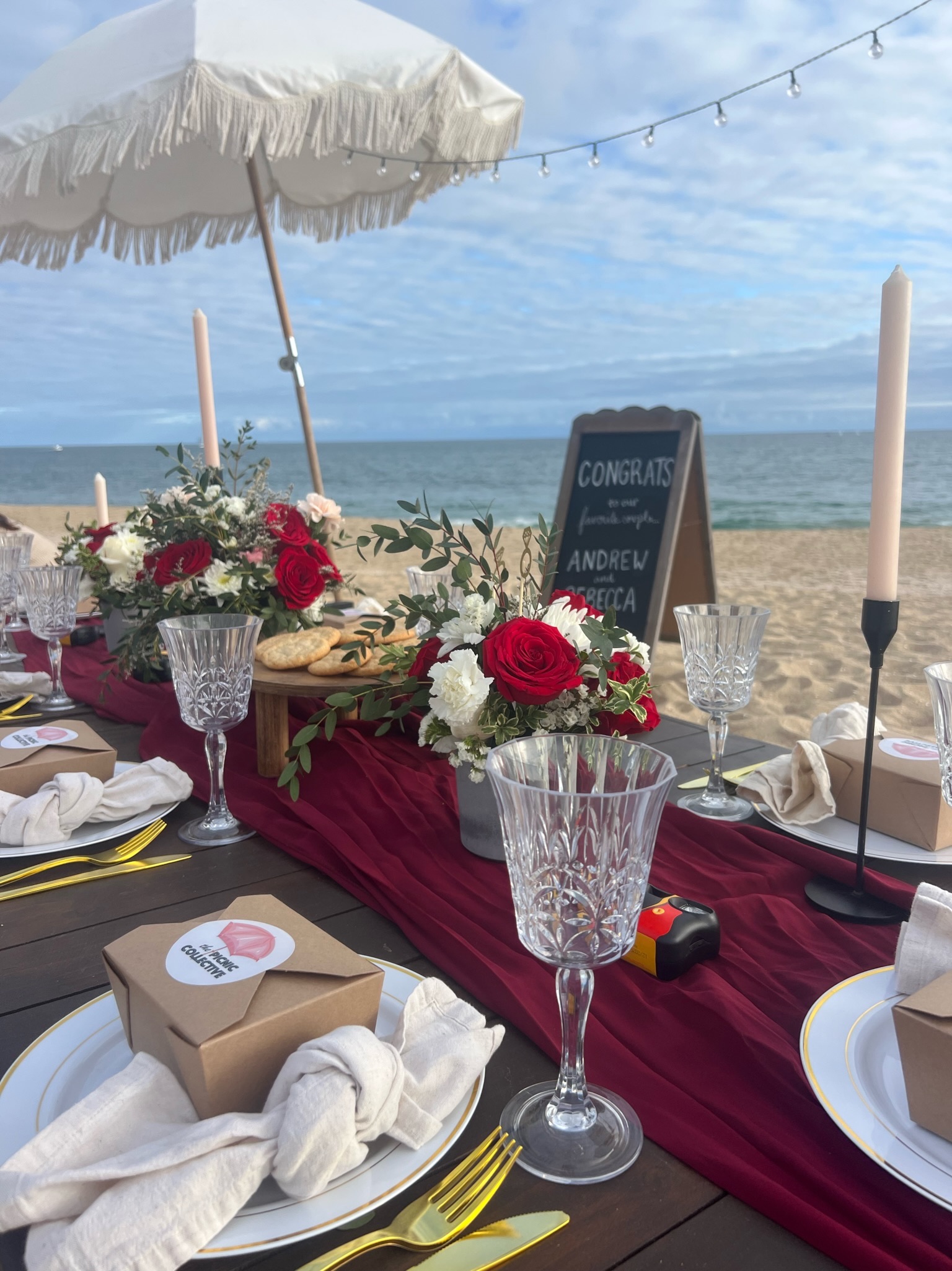 Beach engagement party - elegant table detail with crystal glasses, red florals, and congratulations chalkboard sign