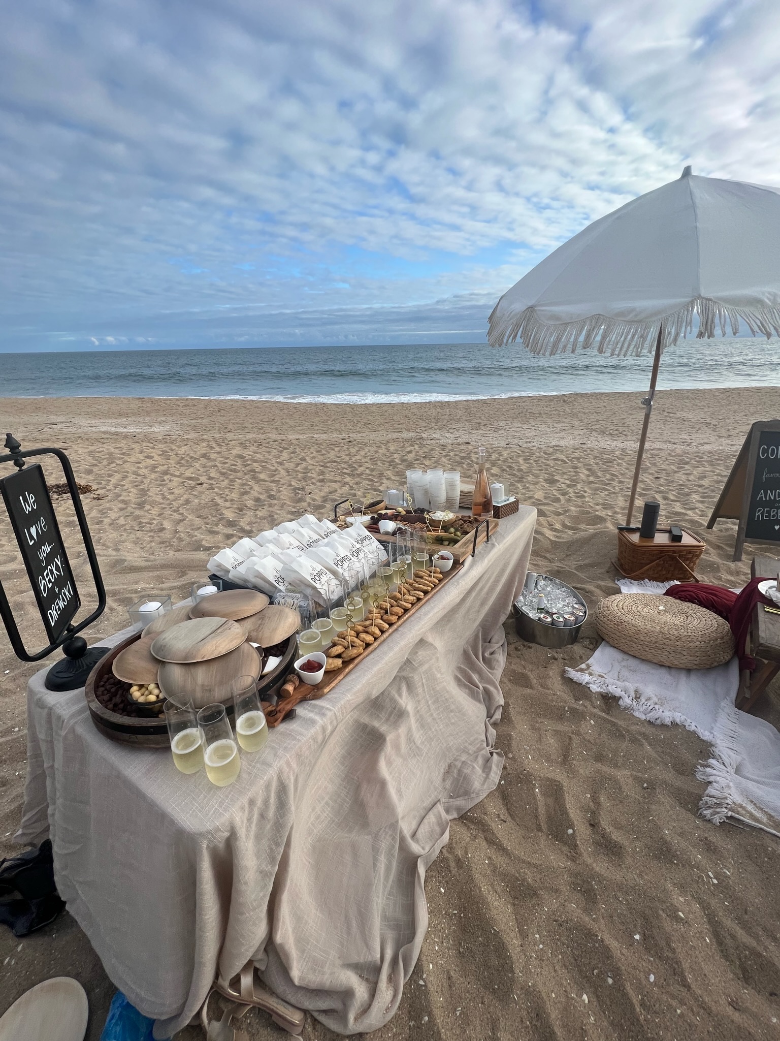 Beach engagement party - wide beach setup with buffet table, champagne glasses, and ocean view