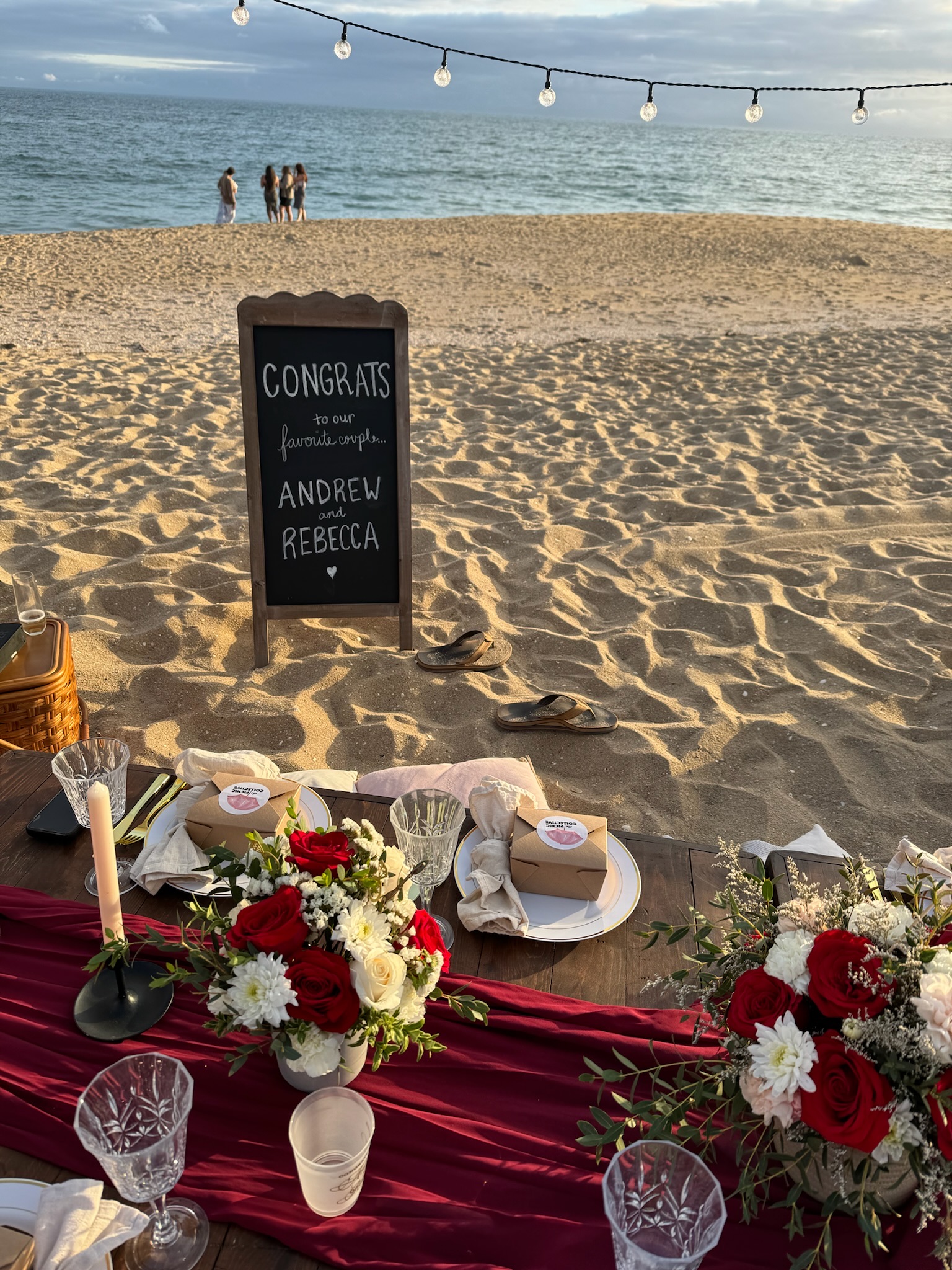 Beach engagement party - elegant table setup at golden hour with congratulations sign and red floral arrangements