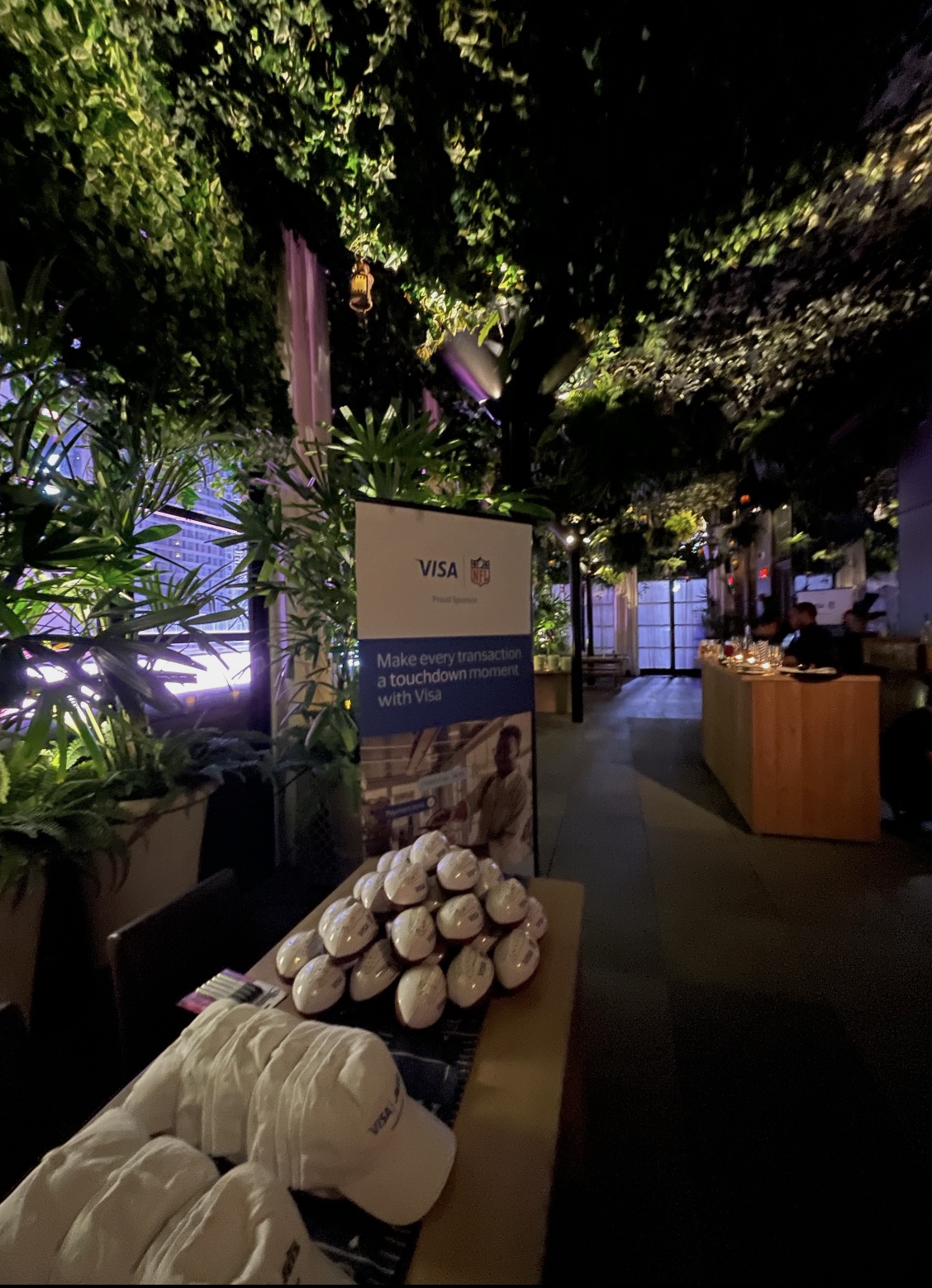Visa NFL activation table with branded footballs and caps under the greenery canopy